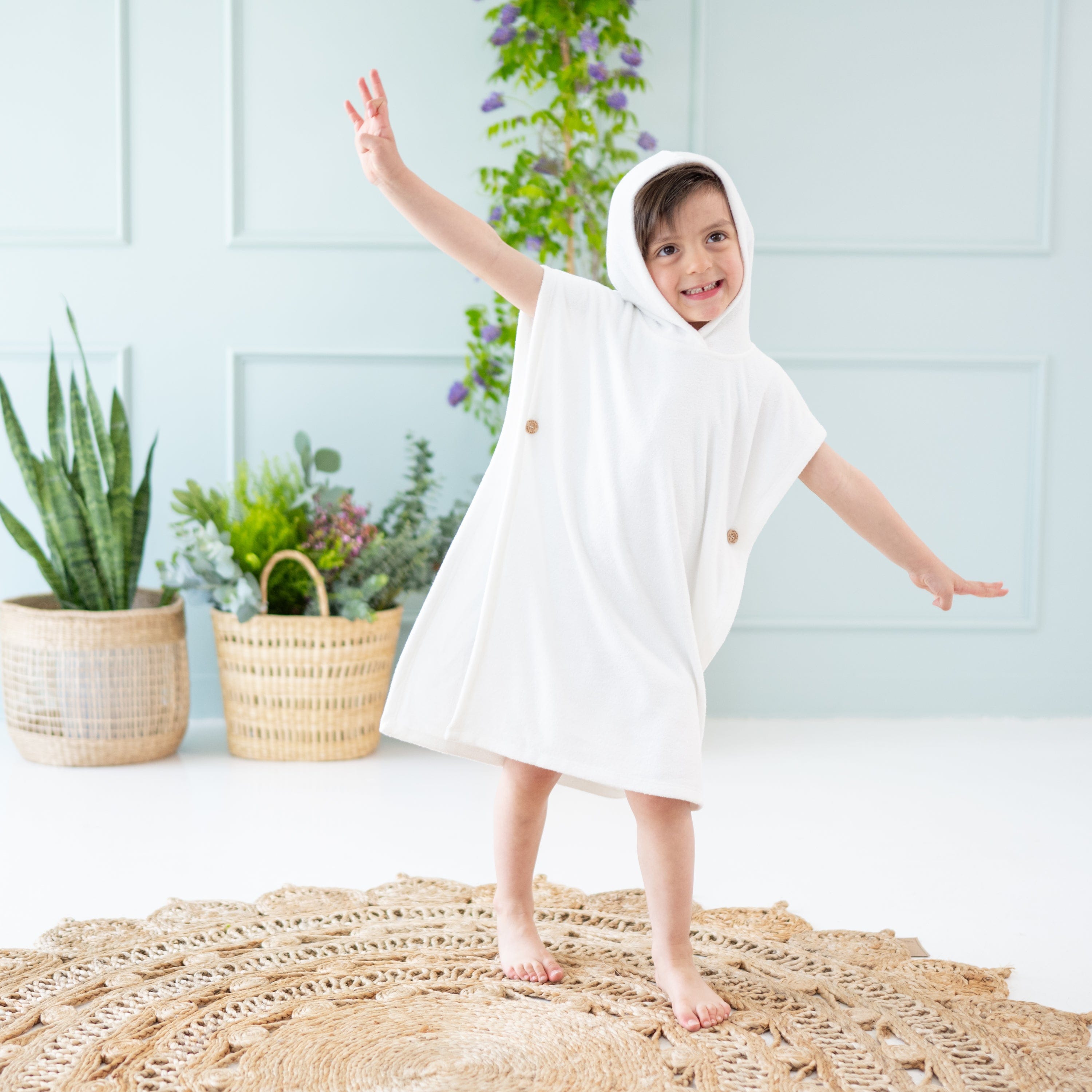 Child wearing Kyte Baby Swim Poncho in Cloud with hood up and plants in background