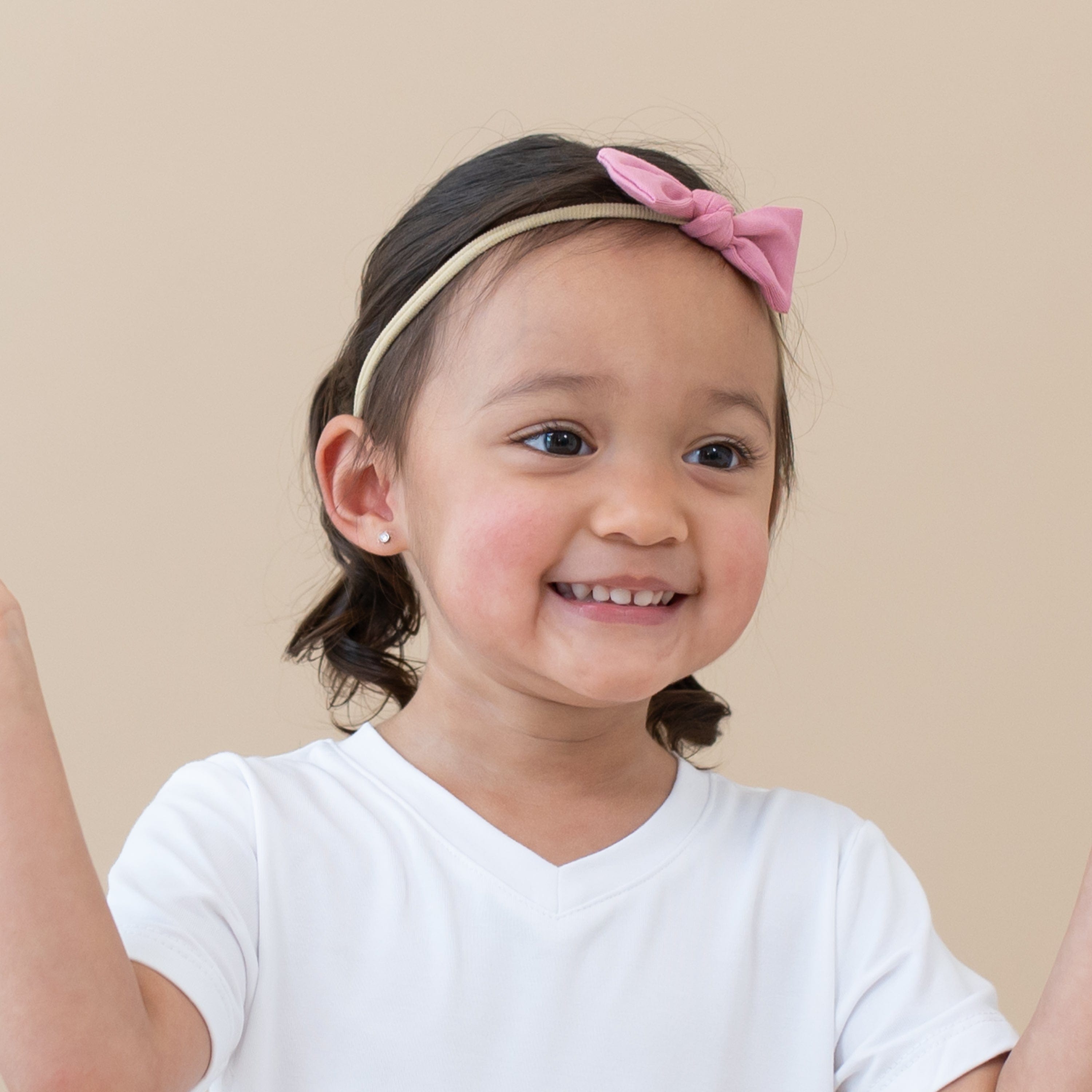 Child wearing Kyte Baby Tiny Bow with Nylon Band in Apple Blossom