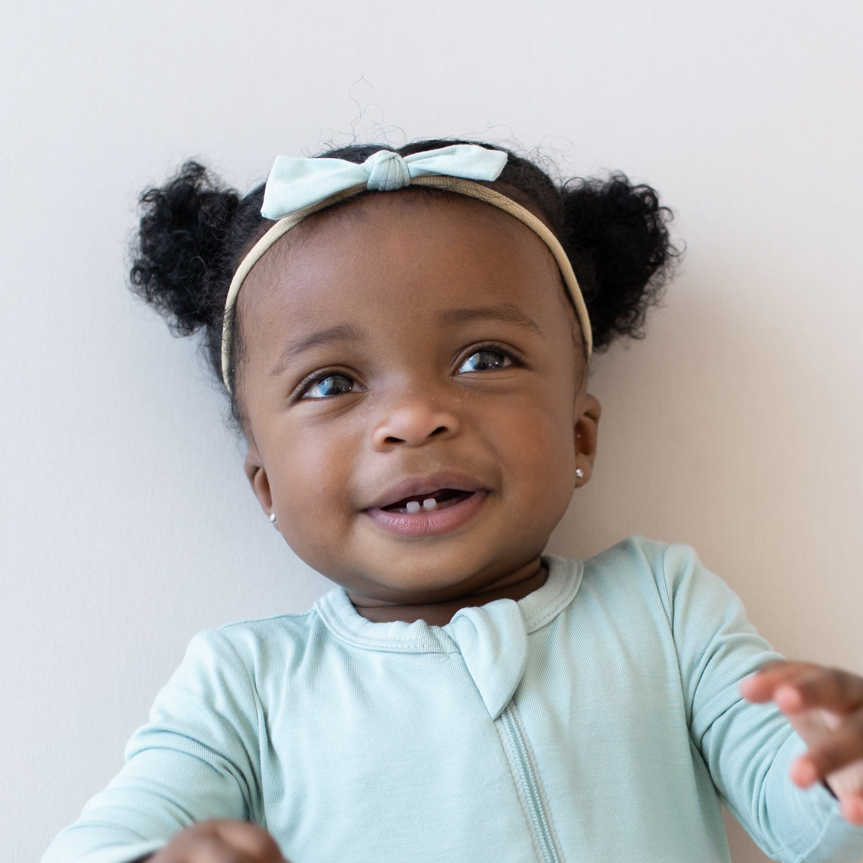 Smiling infant wearing a Tiny Nylon Bow in Sage and matching zippered romper