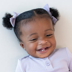 Smiling tddler wearing two Kyte Baby Tiny Nylon Bows in Taro in their pigtails 