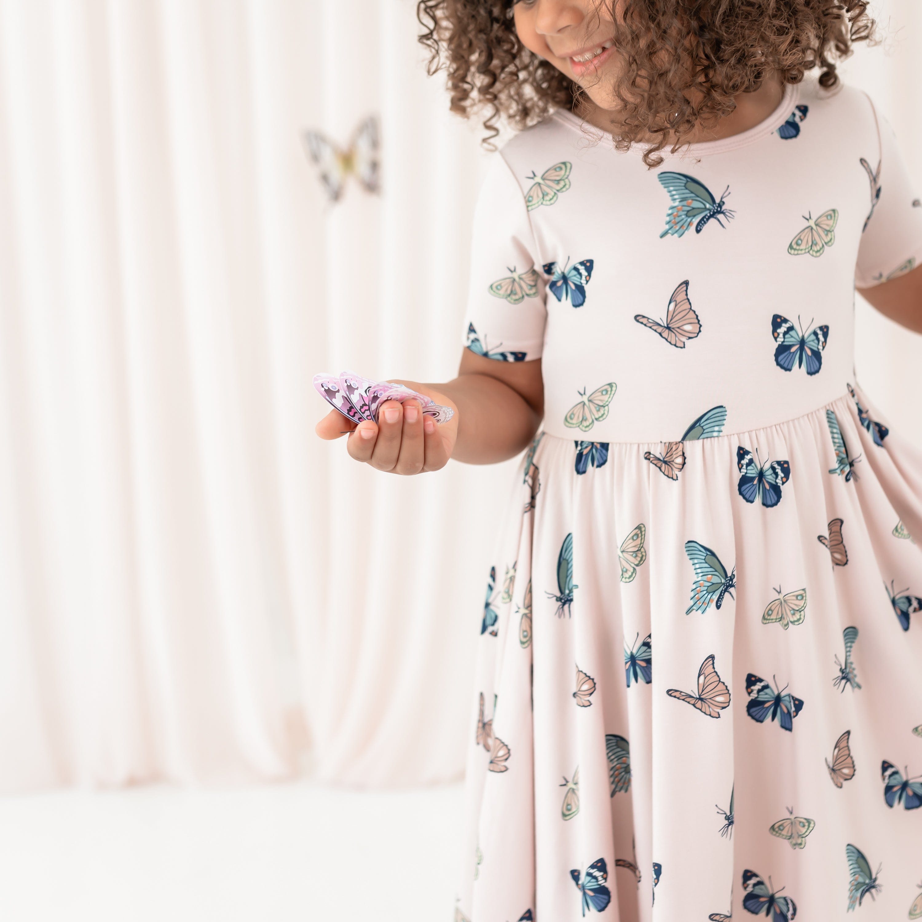 Young girl wearing the Twirl Dress in Blush Butterfly holding a paper butterfly in her hand