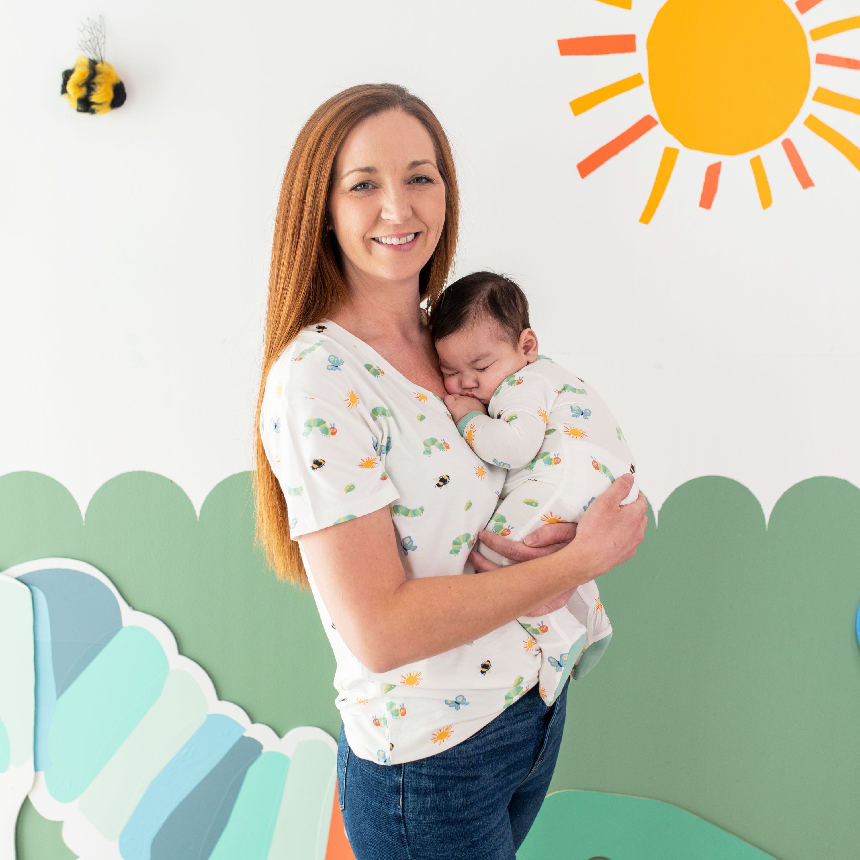 Woman wearing Kyte Baby Women's Relaxed Fit V-Neck in The Very Hungry Caterpillar™ and Friends with Infant in matching footie pajamas