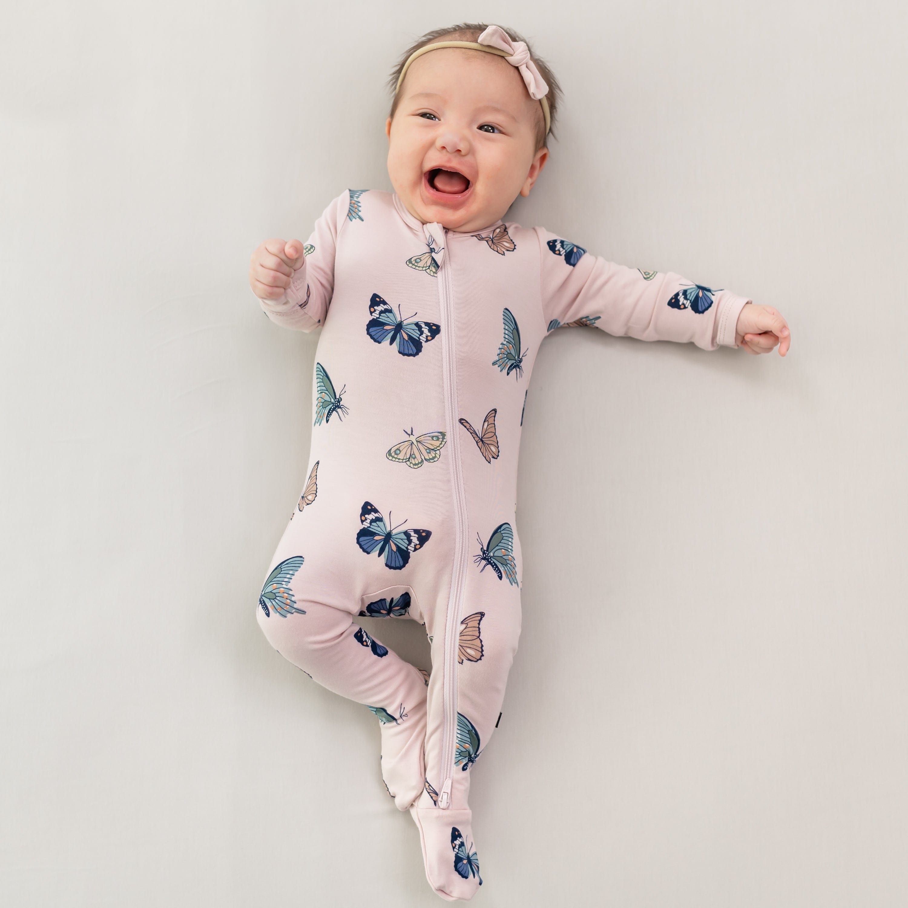 Infant wearing Zippered Footie in Blush Butterfly with pink bow headband