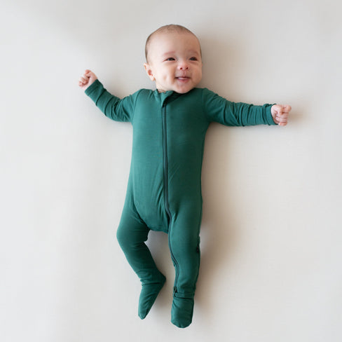 Baby laying on an oat surface and wearing Zippered Footie in Emerald