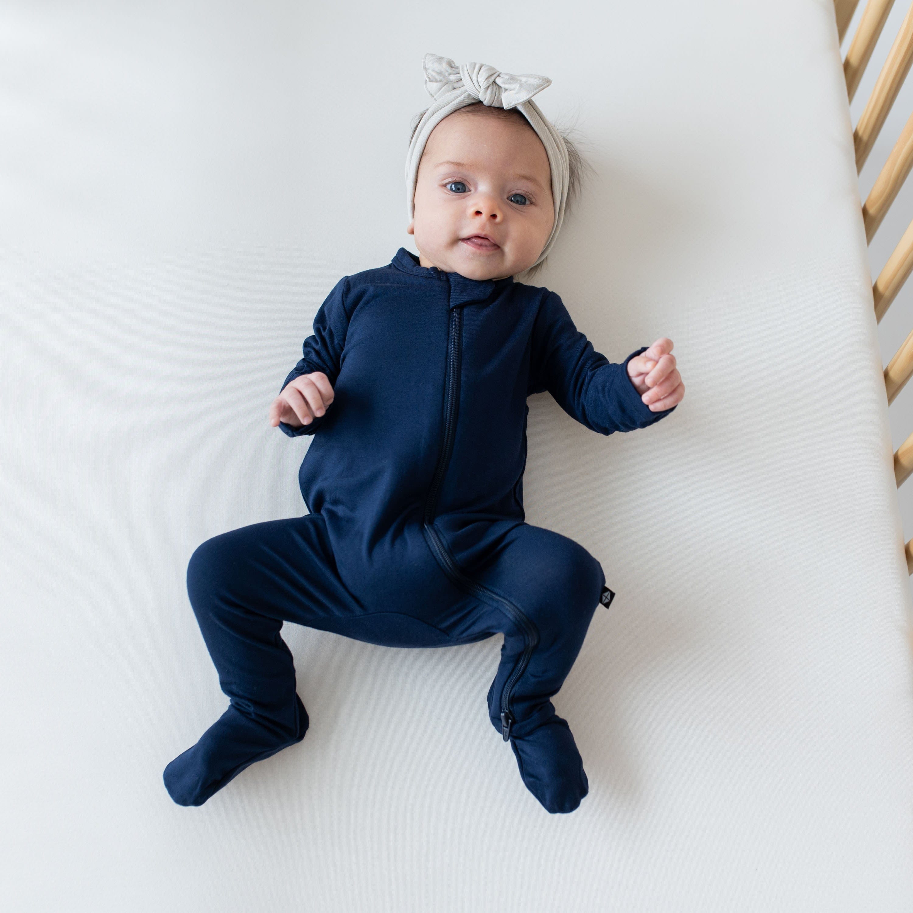 Infant wearing a Zippered Footie in Navy and a headwrap bow in Oat