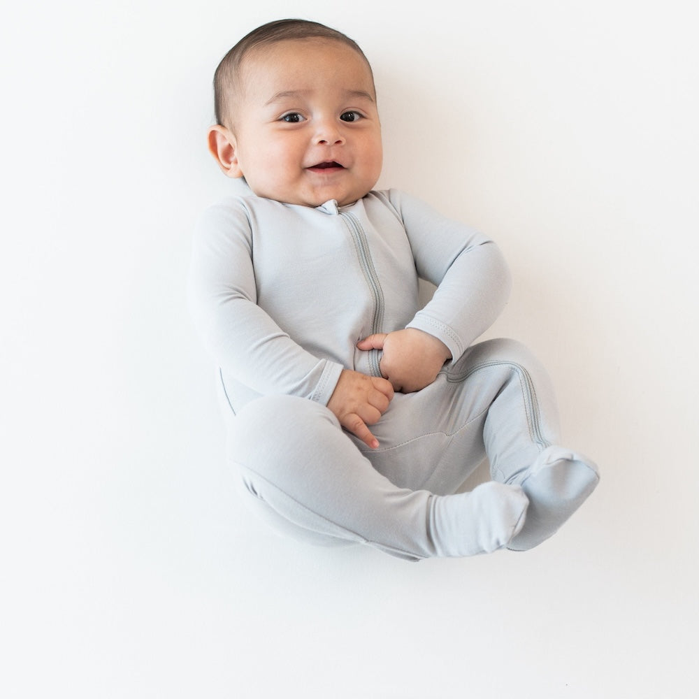 Infant laying down on a crib sheet wearing the Zippered Footie in Storm