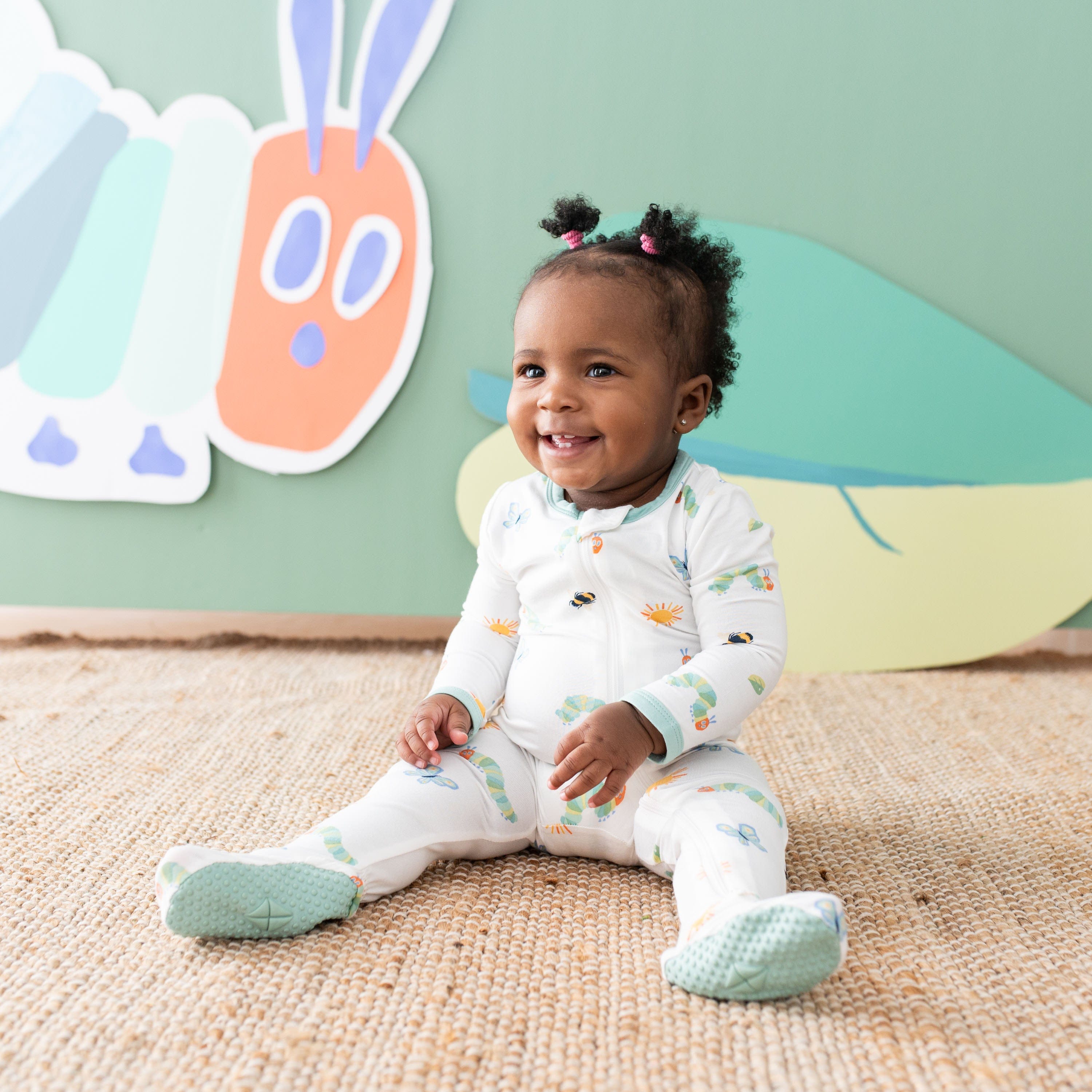 Toddler sitting on the floor wearing the Zippered Footie in The Very Hungry Caterpillar™ and Friends