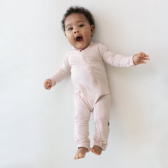 Infant laying on an off-white surface while wearing a Zippered Romper  in Blush