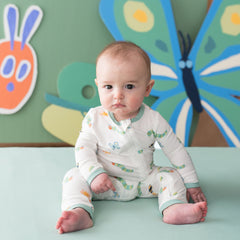 Infant siting on a green crib sheet wearing the Zippered Romper in The Very Hungry Caterpillar™ and Friends