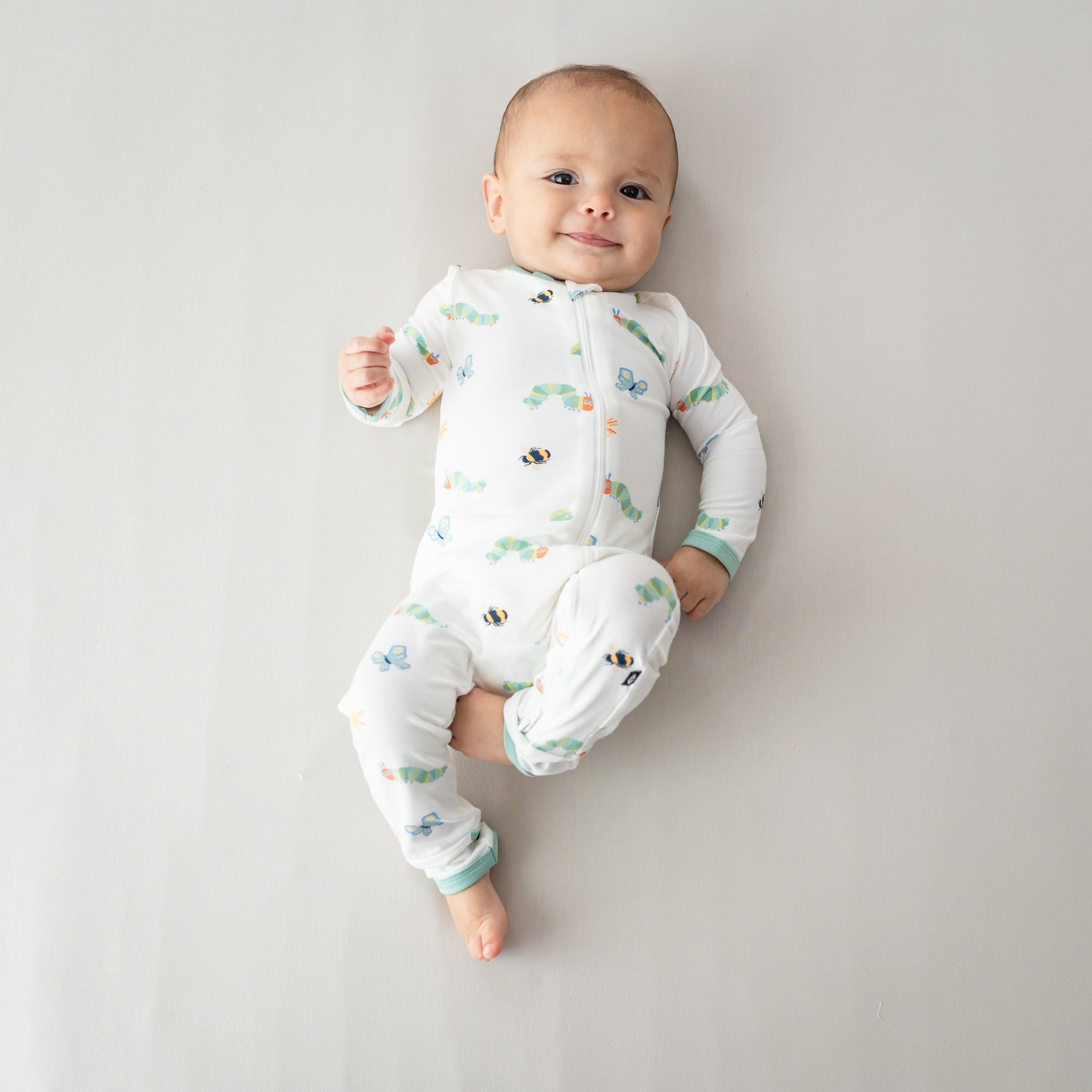 Young infant laying on a light beige blanket wearing the Zippered Romper in The Very Hungry Caterpillar™ and Friends