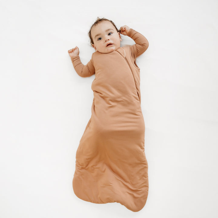 Infant wearing the Sleep Bag in Latte 2.5 with a matching long sleeve romper underneath