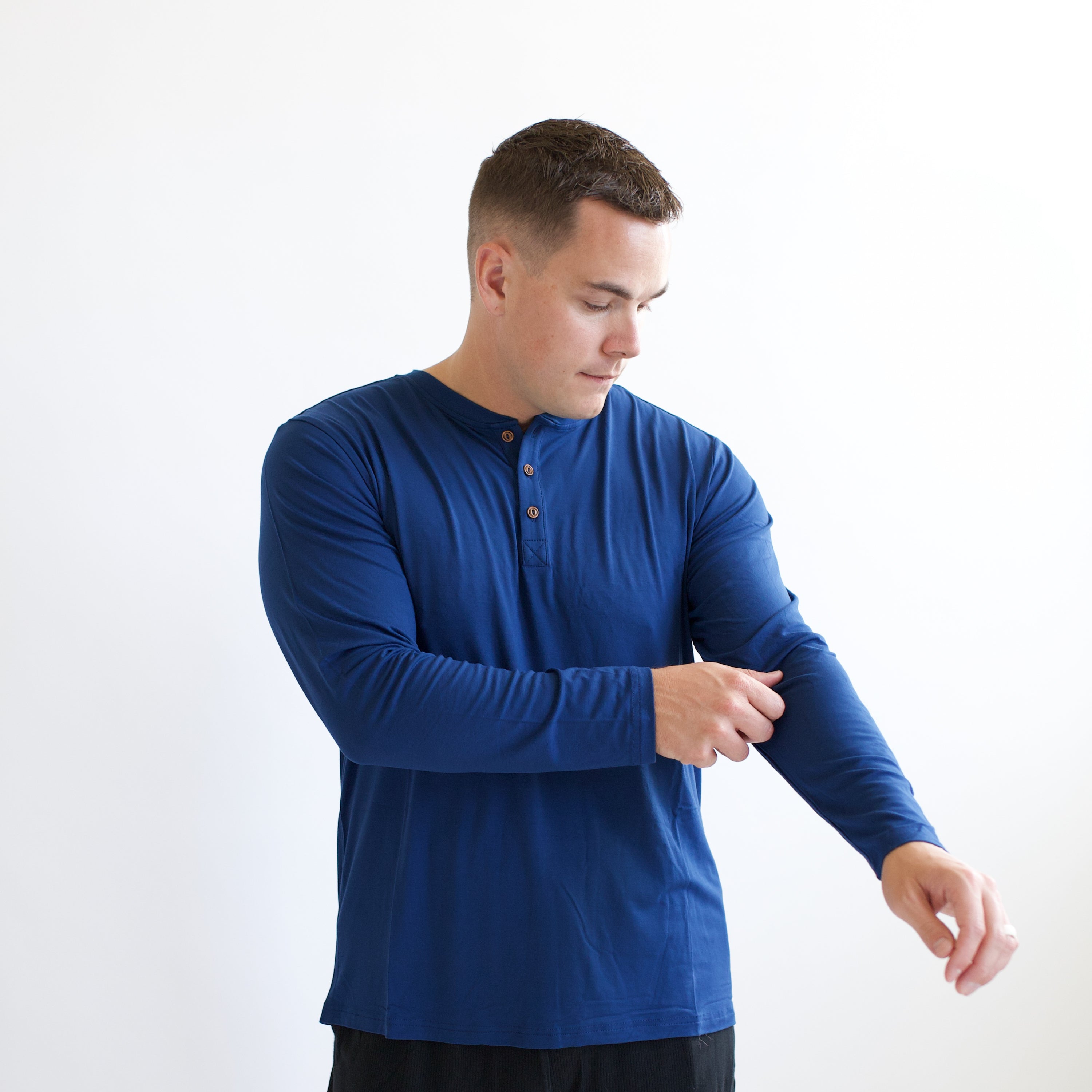 Male model pulling up the sleeve of the Men's Long Sleeve Henley Top in Tahoe standing in front of a white background