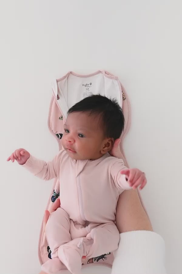 Baby being swaddled in a pink butterfly patterned swaddle bag