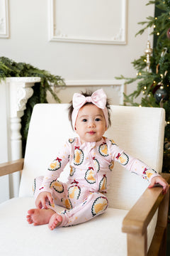 Baby wearing Zippered Romper in Princess Holiday Portraits print and knotted bow headband while sitting on a white sofa