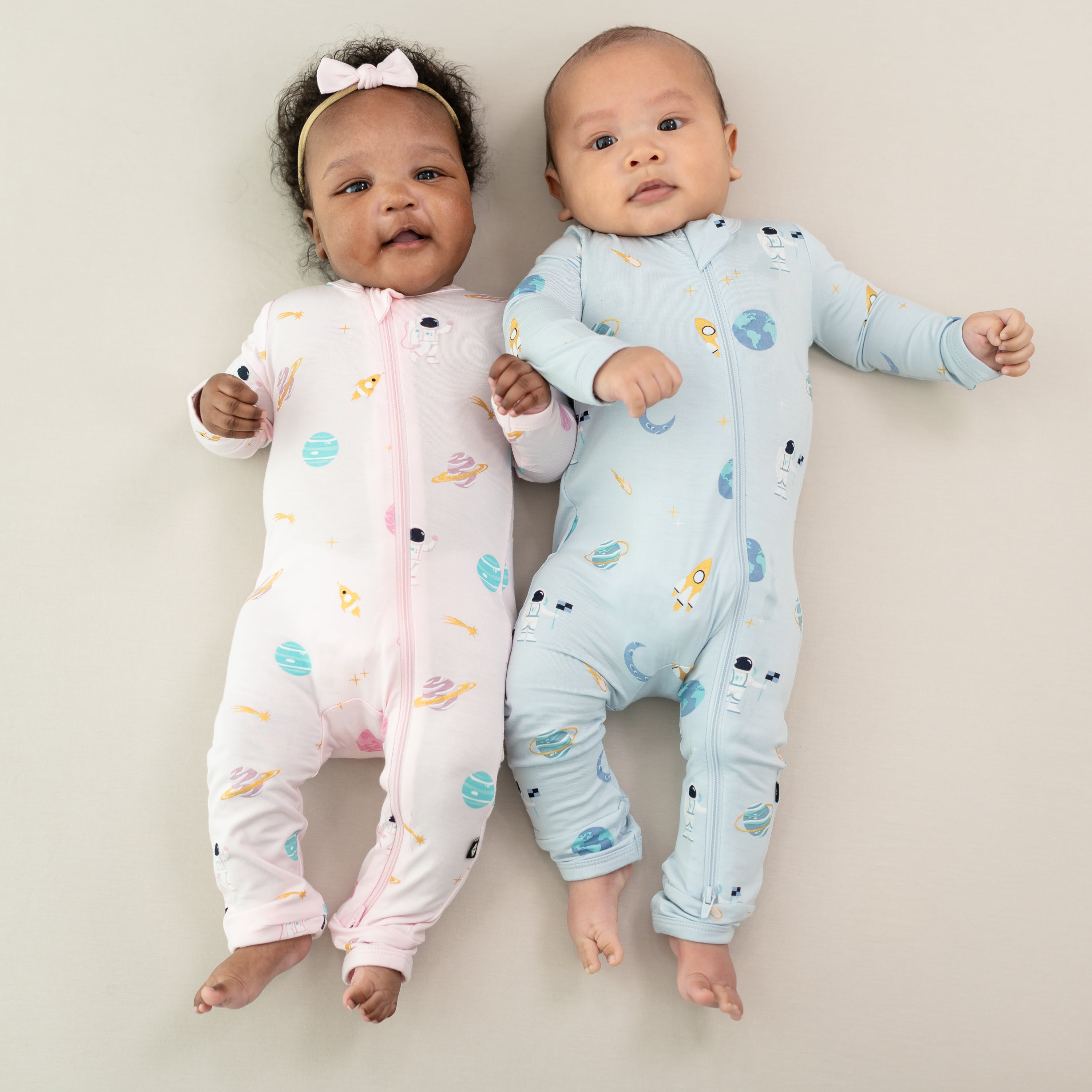 two babies laying wearing zippered rompers in sakura space and ice space