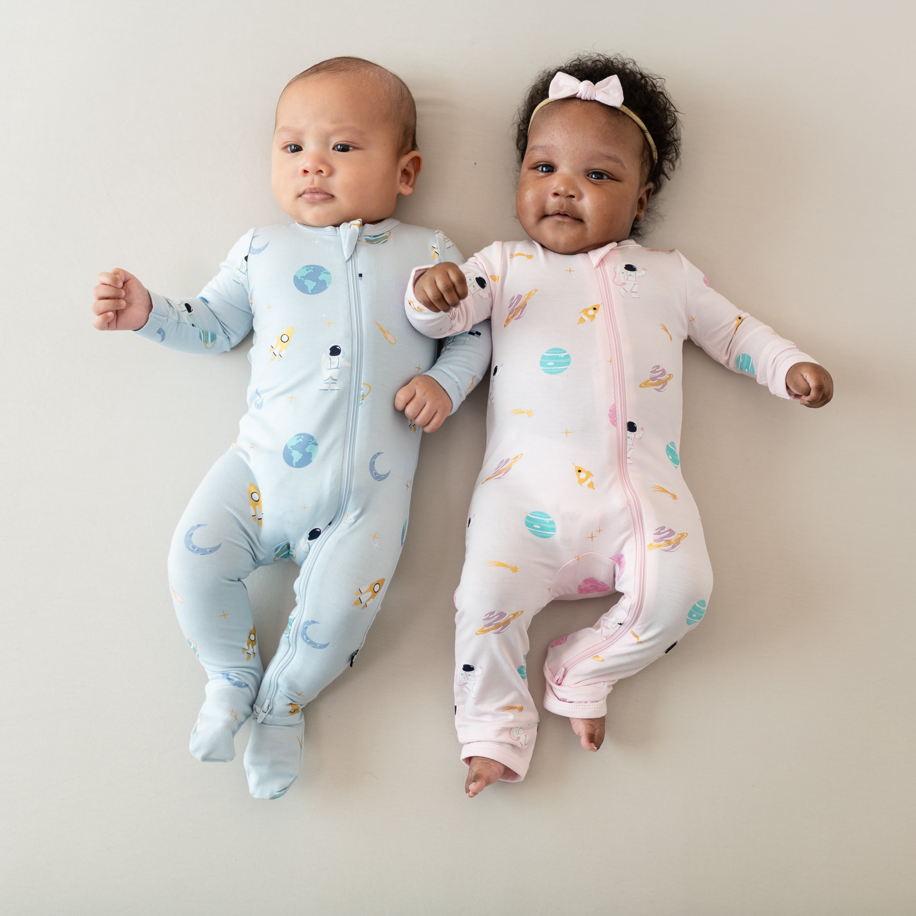 two babies wearing ice space zippered footie and sakura space zippered romper