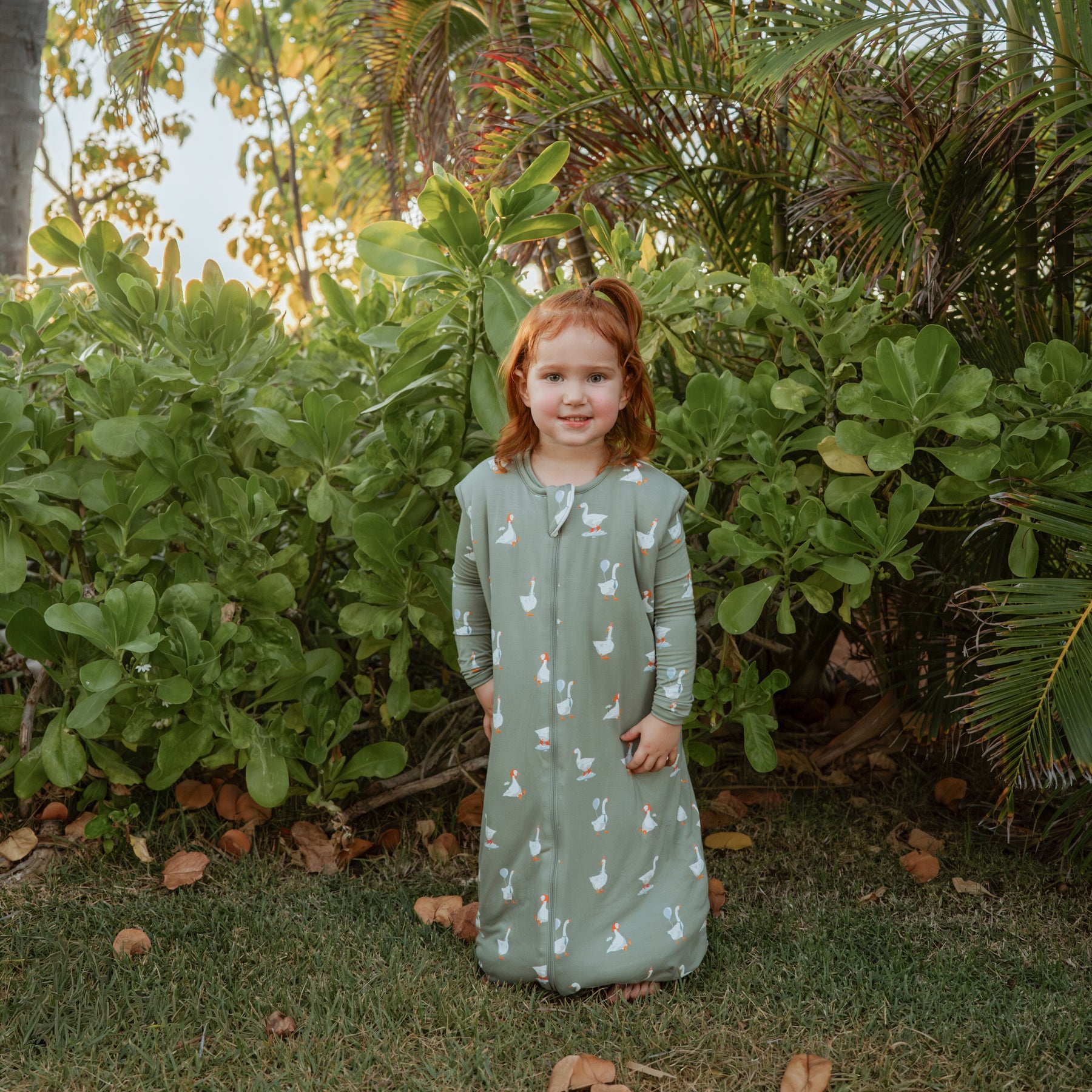 Young girl standing in a field wearing the Sleep Bag Walker in Silly Goose 2.5 with matching long sleeve toddler pajamas on underneath