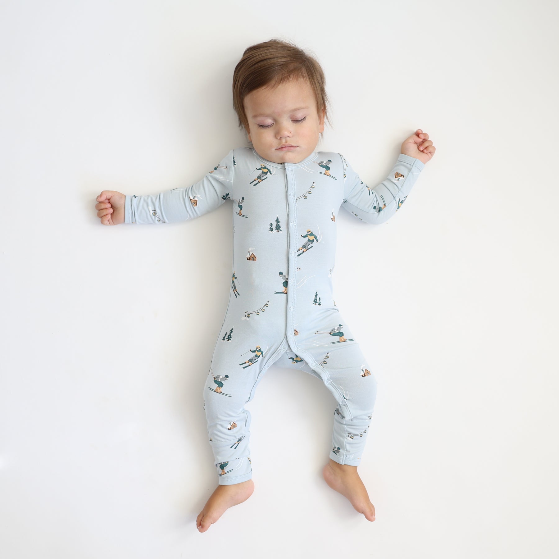 Sleeping toddler laying on a light colored surface wearing the Romper in Ski