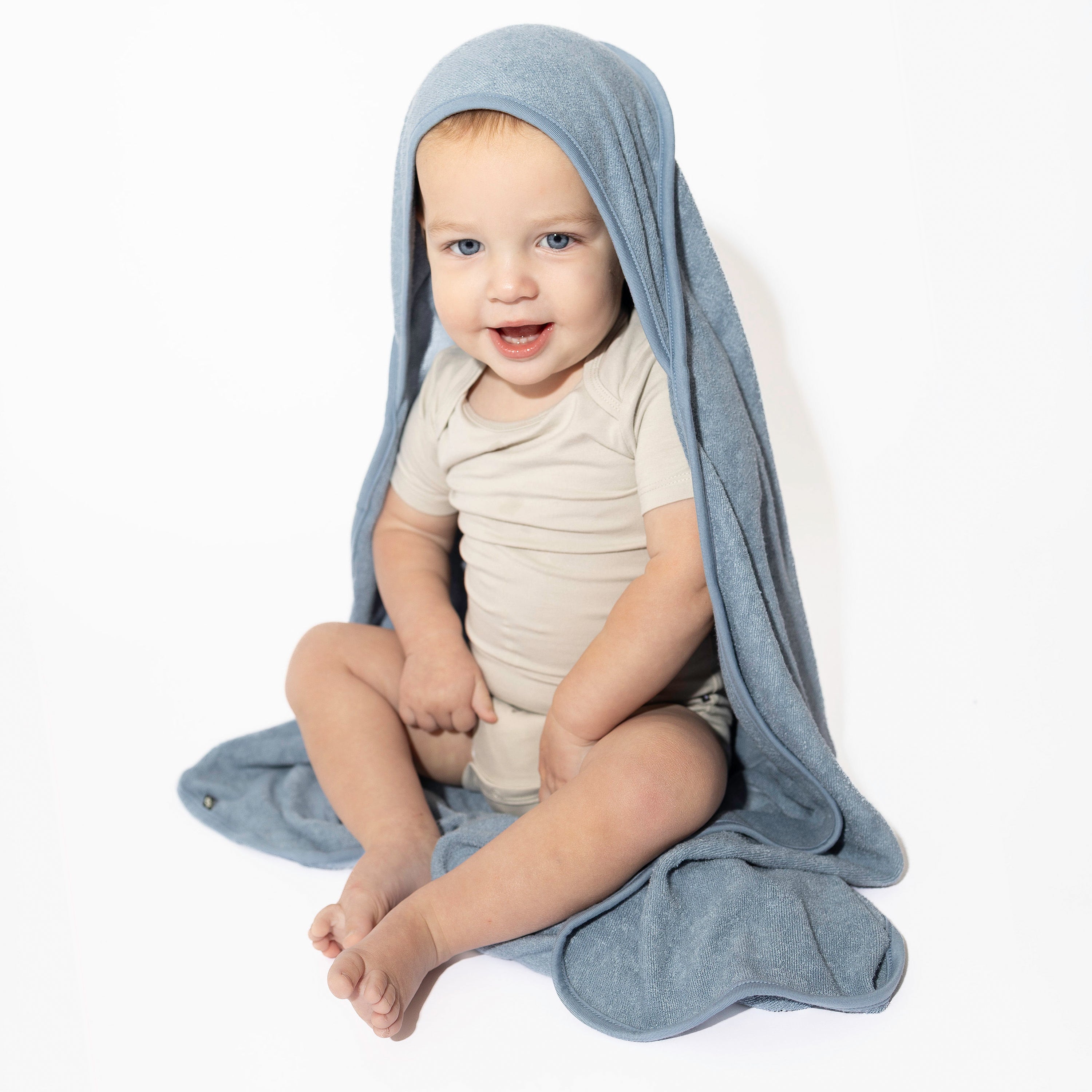Toddler sitting down wearing the Hooded Bath Towel in Slate in front of a white backdrop