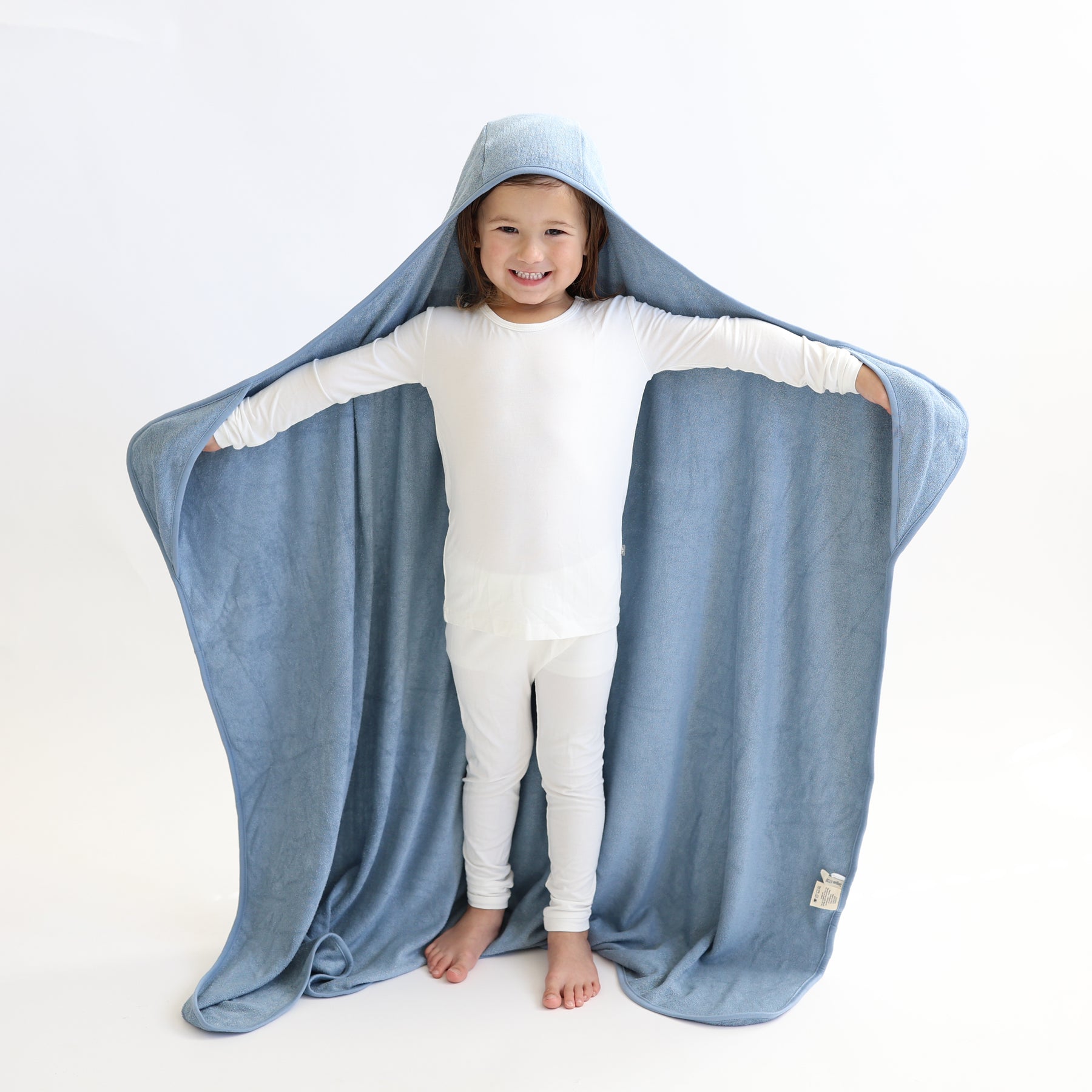 Young girl standing wearing the Toddler Hooded Bath Towel in Slate with her head in the hood and hands in the pockets of the towel