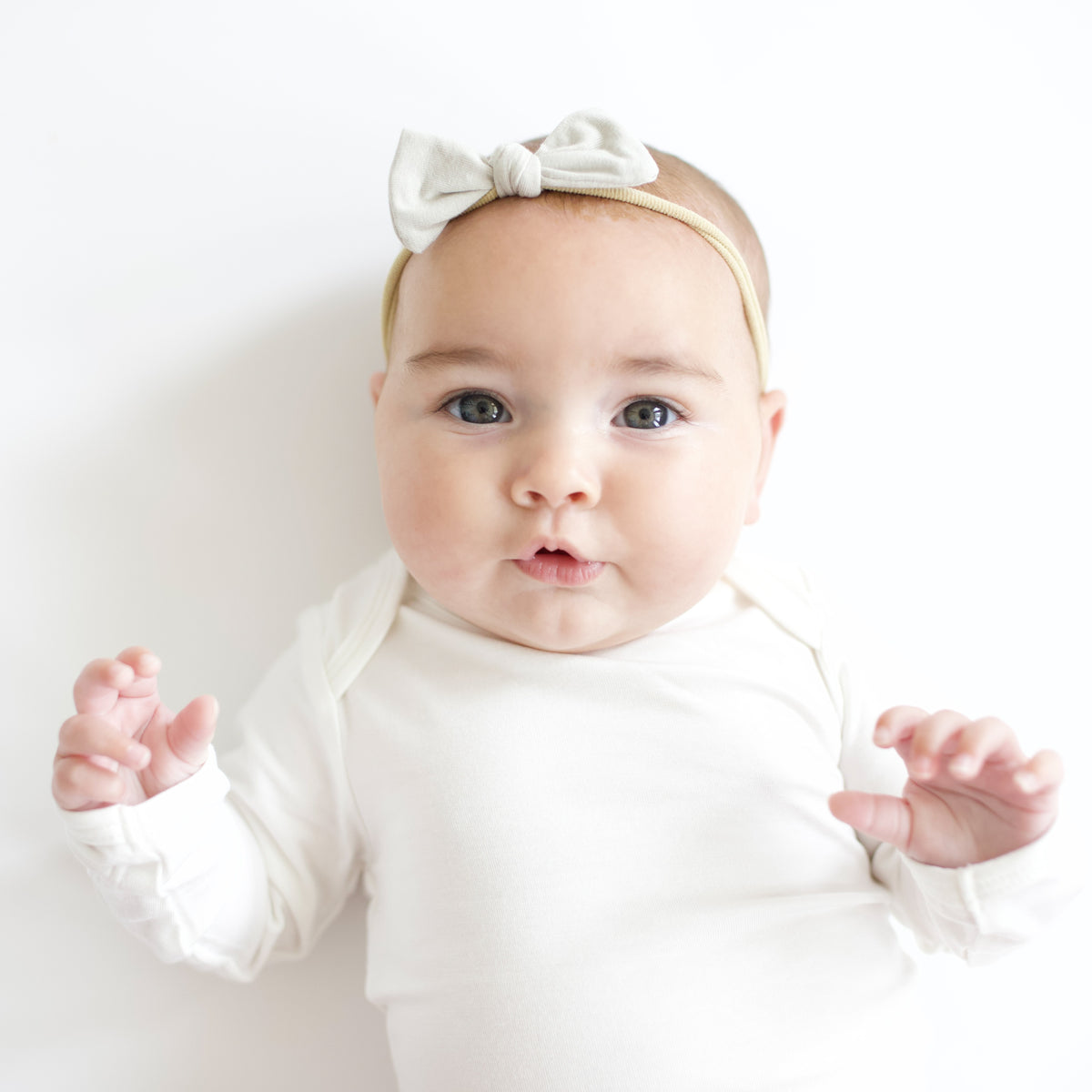 Infant laying down while wearing a Tiny Bow in Oat and Long Sleeve Bodysuit in Cloud
