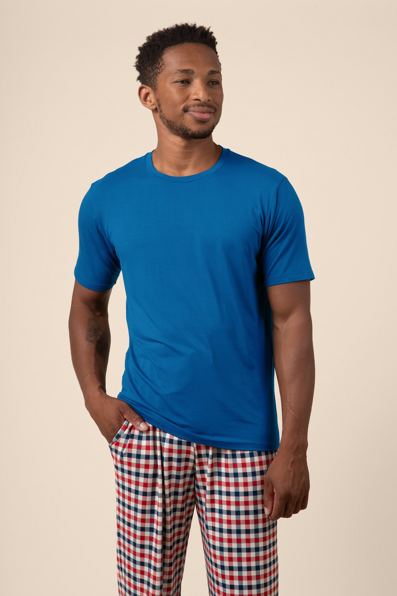 Man wearing a blue t-shirt and red, white, and blue checkered pants on a beige background