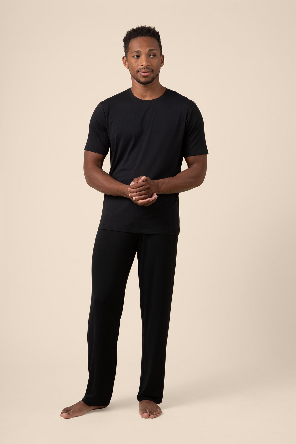 Man wearing a black t-shirt and black pants on a beige background