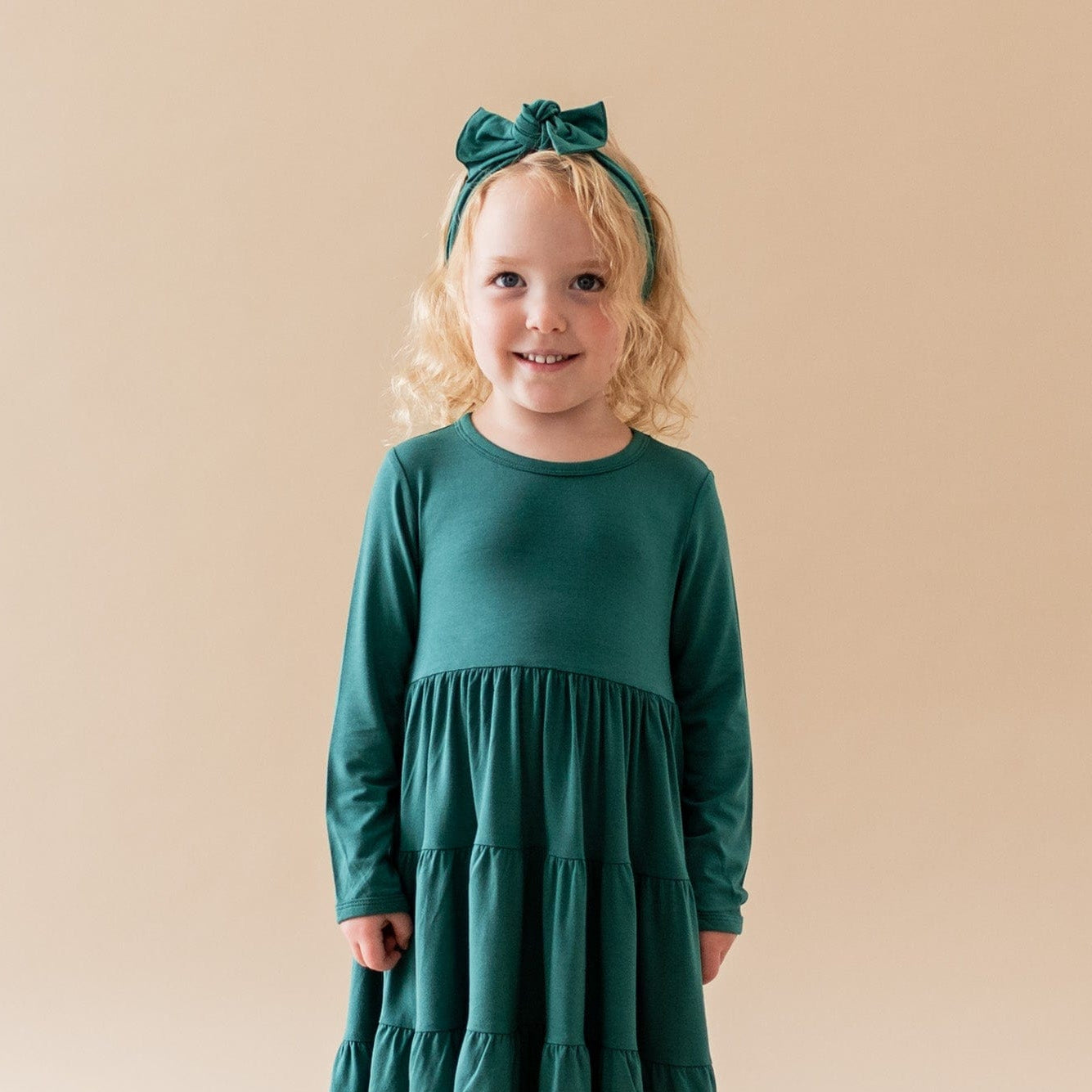 Toddler wearing Kyte Baby Bow headband in Emerald green with matching tier dress
