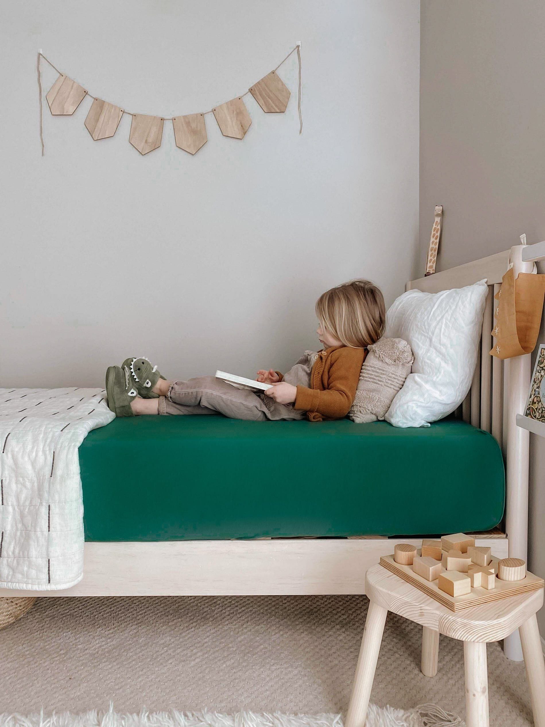 Child sitting on bed with Corner of Kyte Baby Twin Sheet in Emerald