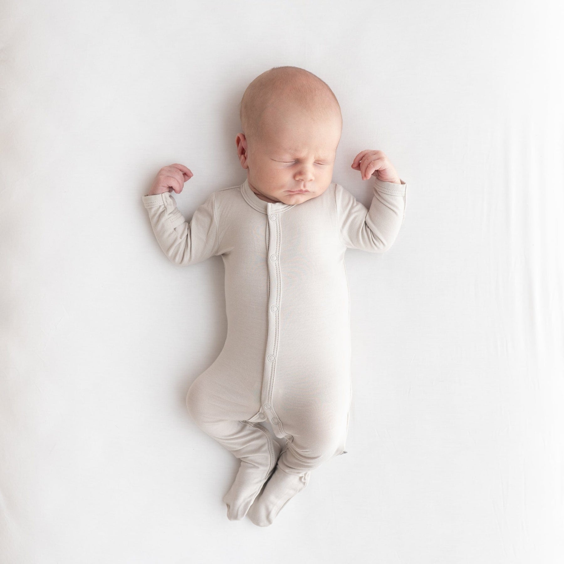 Infant wearing Kyte Baby Snap Footie pajamas in Oat