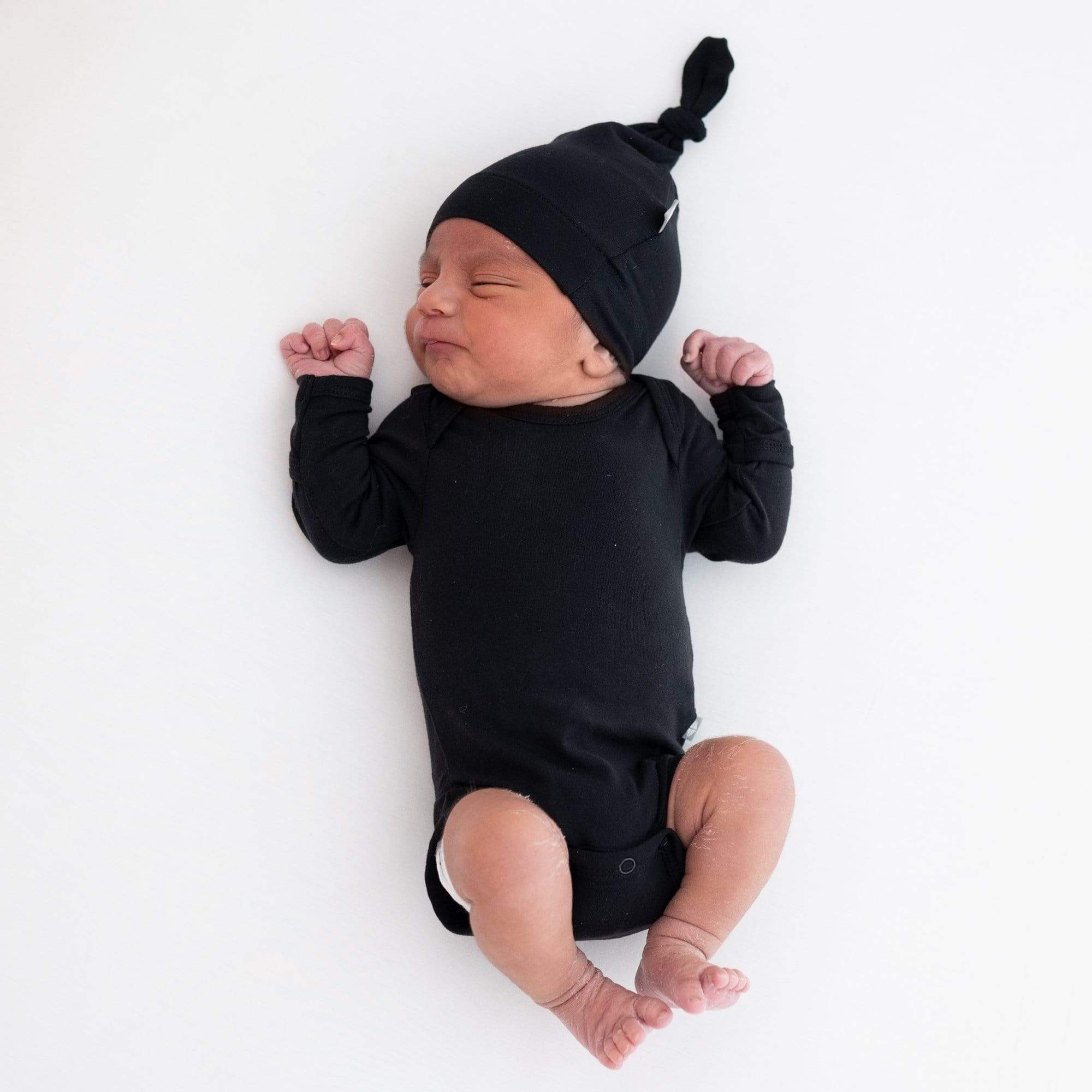 Newborn wearing Kyte Baby bamboo Long Sleeve Bodysuit in Midnight black with matching hat