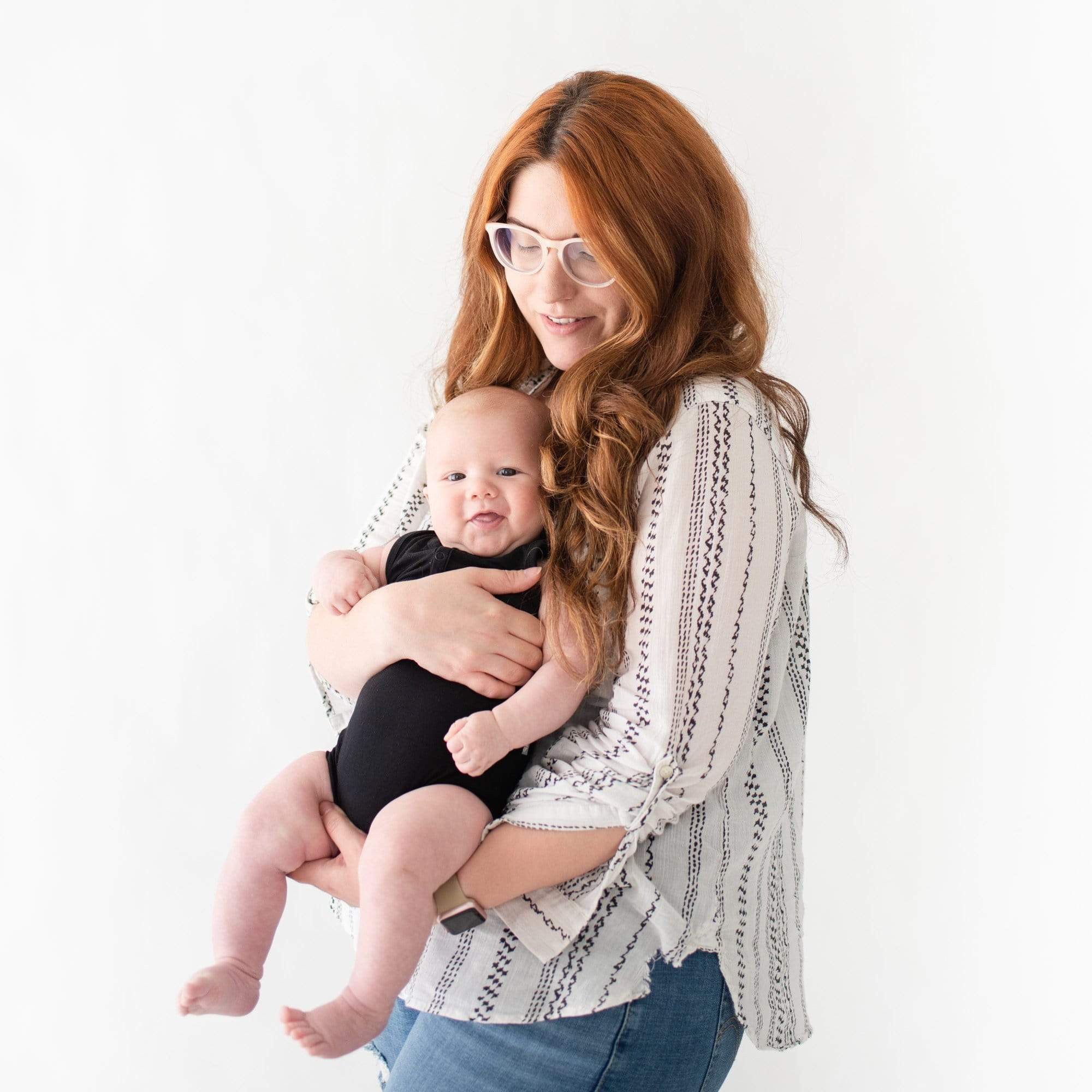 Mom holding infant wearing Kyte Baby Sleeveless Bodysuit in Midnight