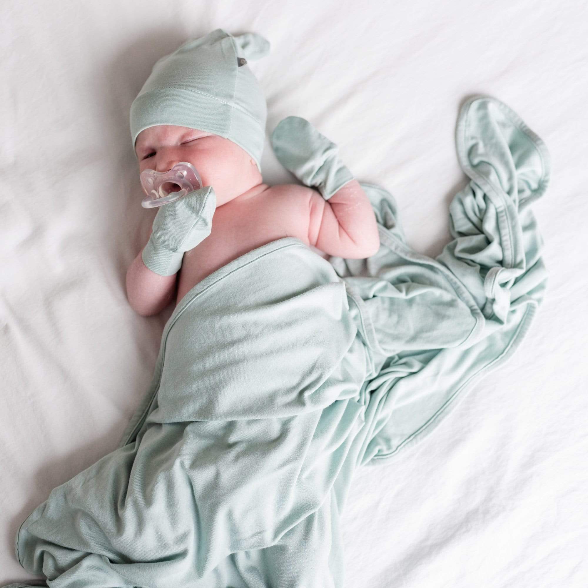 Newborn covered with in Kyte Baby Swaddle Blanket in Sage