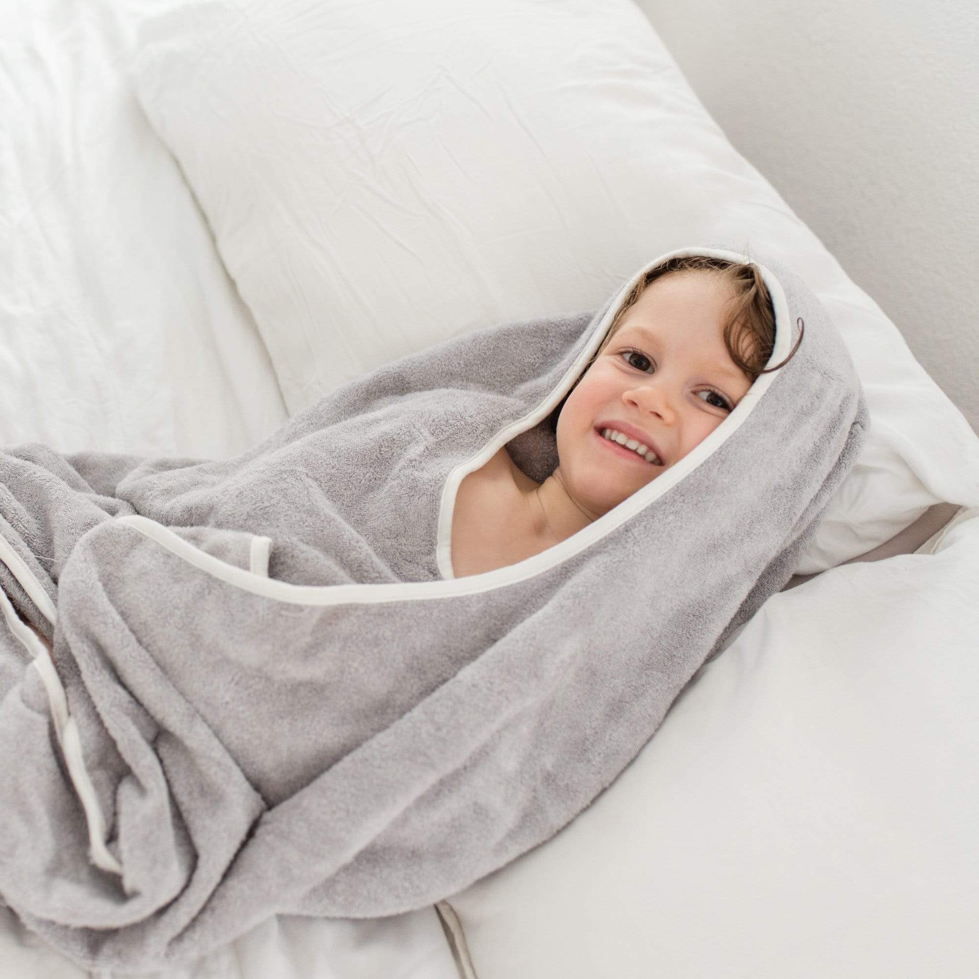 Toddler wrapped in Kyte Baby Hooded Bath Towel in Storm with Cloud Trim